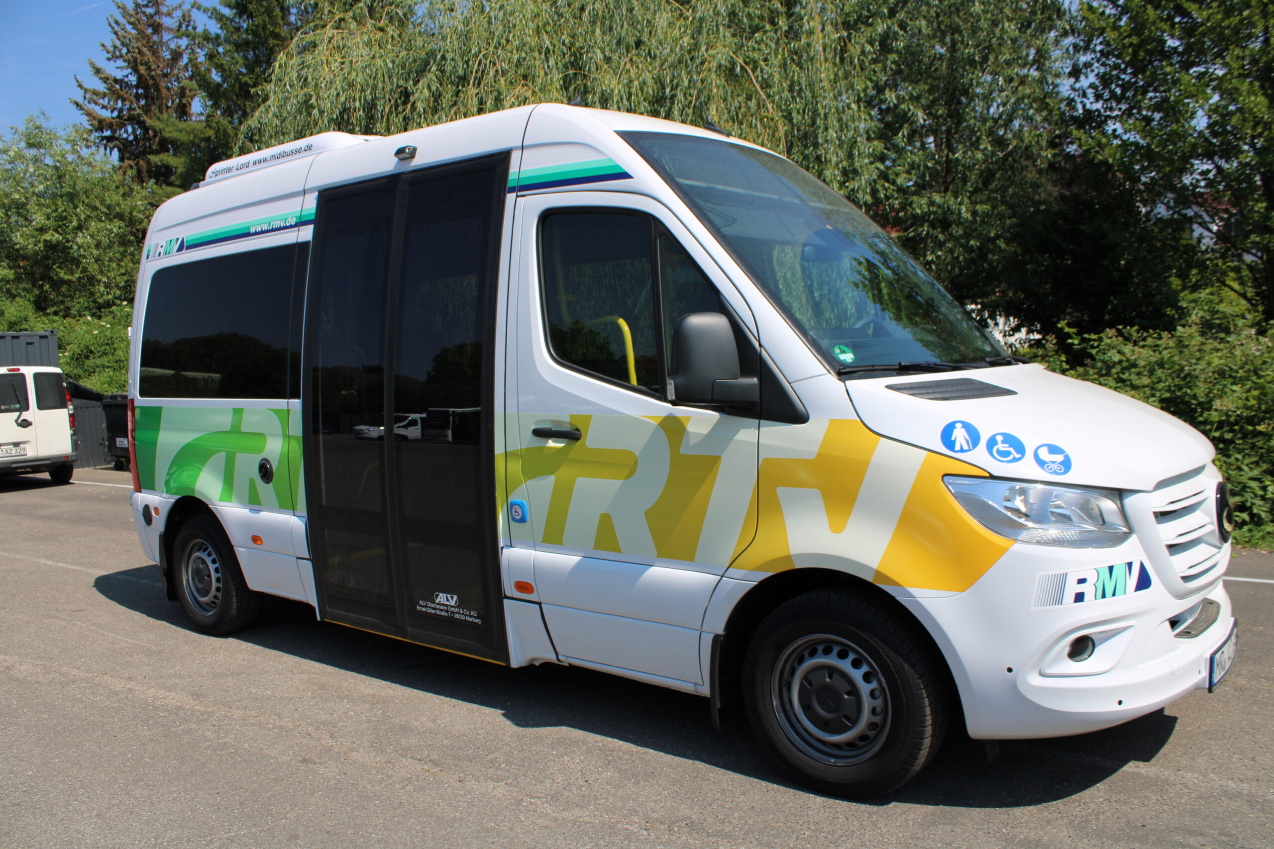 Ein barrierefreier Rufbus der Rheingau-Taunus-Verkehrsgesellschaft mit RMV-Branding steht auf einem Parkplatz. Der weiße Kleinbus ist mit gelb-grüner „RTV“-Beklebung versehen und zeigt Piktogramme für mobilitätseingeschränkte Fahrgäste, Kinderwagen und Fahrräder.